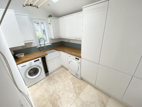 a kitchen with white cabinets and a washer and dryer at Trewhiddle Retreat V9 by Together Travel - Luxury 4-Bedroom Villa in St Austell