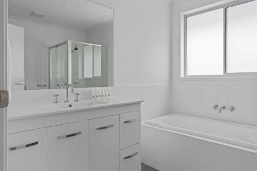 a white bathroom with a tub and a sink and a mirror at Wine Down 700m walk to Cessnock CBD in Cessnock