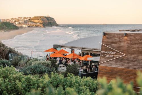 a restaurant with orange umbrellas next to the ocean at Hilltop Hideaway Family Escape in Merewether