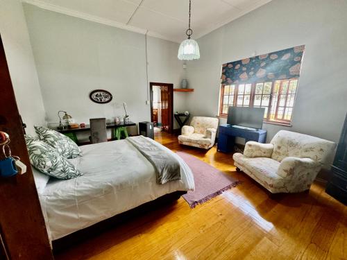 a bedroom with a bed and two chairs and a television at Whistlewood Guesthouse Walmer, Port Eizabeth in Port Elizabeth