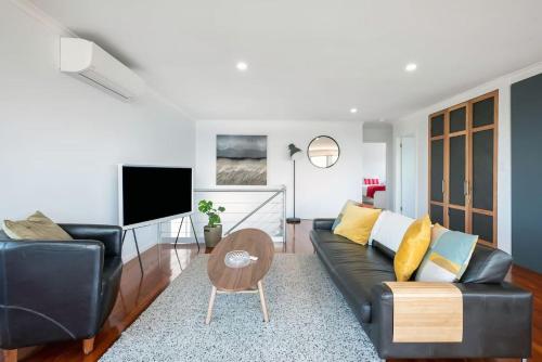 a living room with a black couch and a tv at Stunning Coastal Home Views 1 Hour From Sydney in Wombarra
