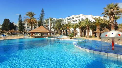 a large swimming pool in a resort with palm trees at Hotel Marhaba Beach in Sousse