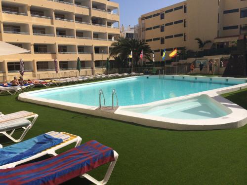 a large swimming pool with green grass next to a building at Apartamentos Amazonas in Playa del Ingles