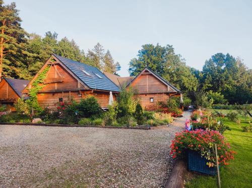 a large wooden house with flowers in front of it at Woodorf drewnem usłane - domki z bala nad rzeką Słupią wśród pól i lasów z chatą grillową, ogniskiem i placami zabaw dla dzieci -Royal Red House z jacuzzi i ogrodzonym extra ogródkiem dla piesków, Royal Green House - bez jacuzzi in Ustka