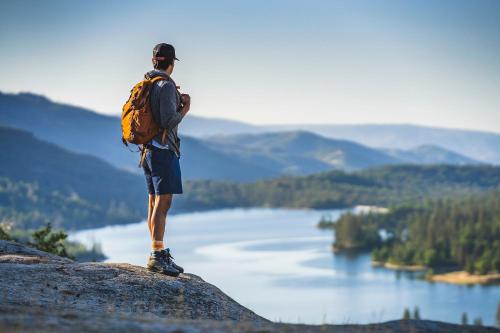 a man with a backpack standing on a rock overlooking a lake at The Pines Resort & Conference Center in Bass Lake