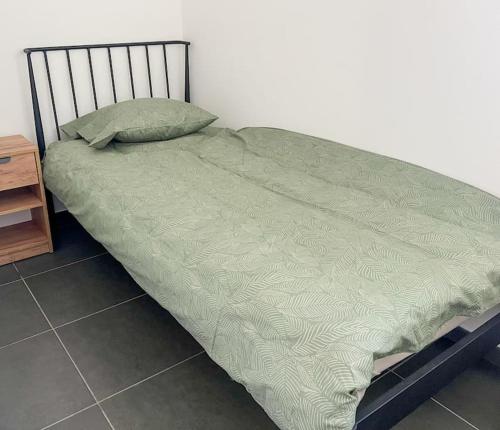 a bed with a green comforter and a night stand at Charmant Logement Brugelette Proche de Pairi Daiza in Brugelette