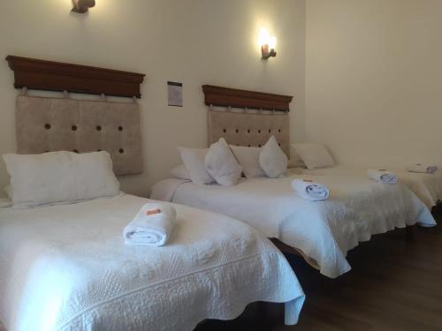 three beds in a room with white sheets at Hotel las Palmas in Villa de Leyva