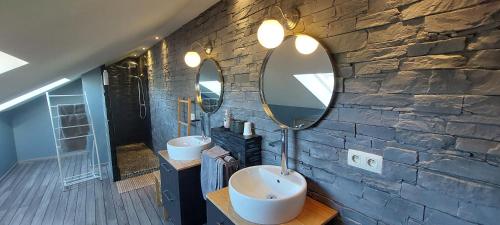 a bathroom with two sinks and two mirrors on a stone wall at Les Champs aux Boules Ambiance très cosy in Herbeumont