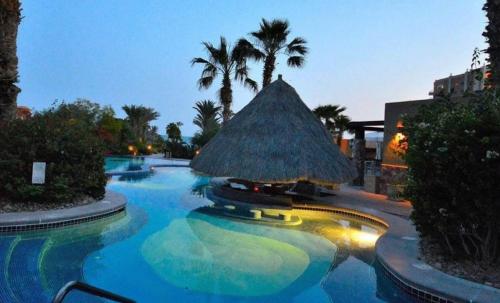 a large swimming pool with a straw umbrella and palm trees at Bella Sirena Resort Premium View Condo in Puerto Peñasco