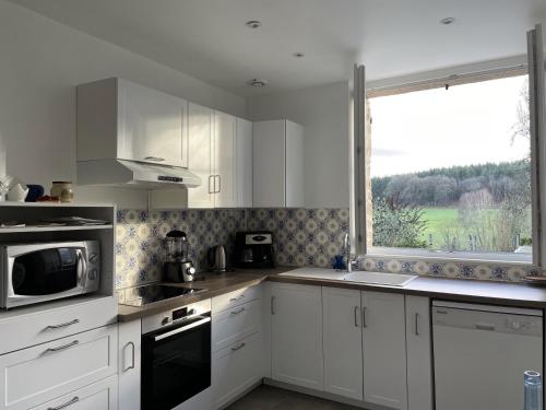 une cuisine avec des placards blancs et une grande fenêtre dans l'établissement Belle vue - Charmante maison Normande au calme, à Rânes