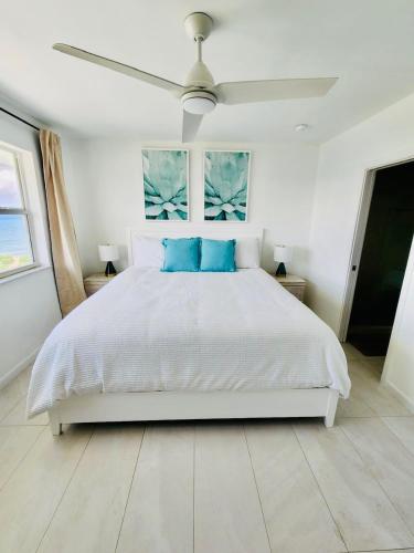 a white bedroom with a white bed with blue pillows at 7Mile Beachfront Apartment in George Town