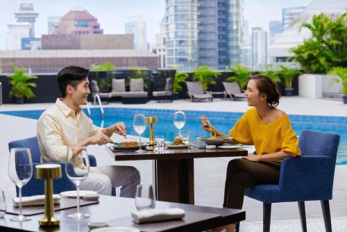 a man and woman sitting at a table eating food at voco Orchard Singapore by IHG in Singapore