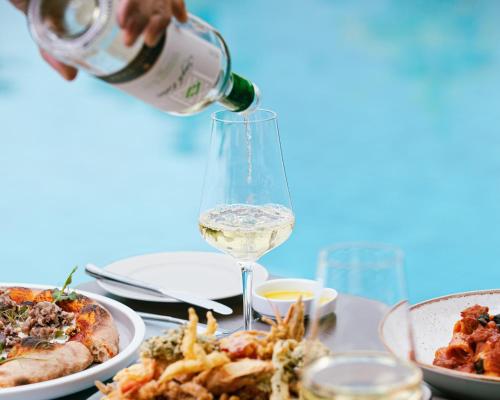 a person pouring white wine into a wine glass at voco Orchard Singapore by IHG in Singapore