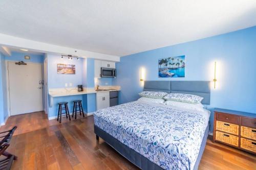 a bedroom with blue walls and a bed and a kitchen at Trendy Studio in the Heart of Honolulu - 21F in Honolulu
