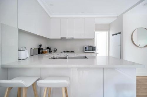 a white kitchen with white cabinets and white stools at The Newtowner - In the Heart of Newtown! in Sydney