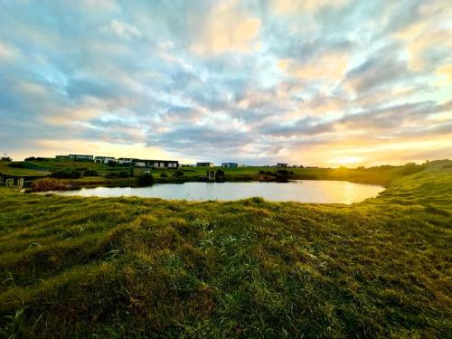 a small pond in a field with a cloudy sky at Luxury Absolute Ocean View Lodge in Waverley
