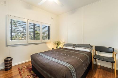 a bedroom with a bed and a chair and two windows at Sharon - Pet Friendly Beach Cottage in Town in Yamba