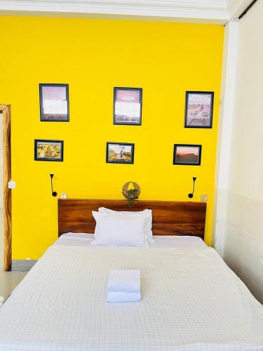 a bedroom with a white bed with a yellow wall at Por Chey Guesthouse in Battambang