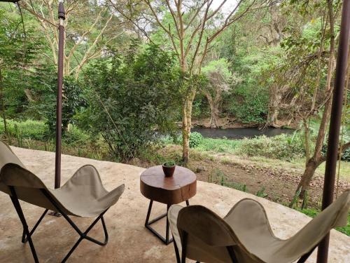 a patio with chairs and a table and a view of a river at Dolly Farm & River Camp, Luxury Tents in Usa River