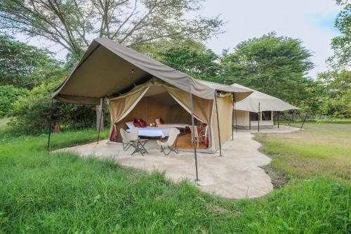 a tent with a table and chairs in a field at Dolly Farm & River Camp, Luxury Tents in Usa River