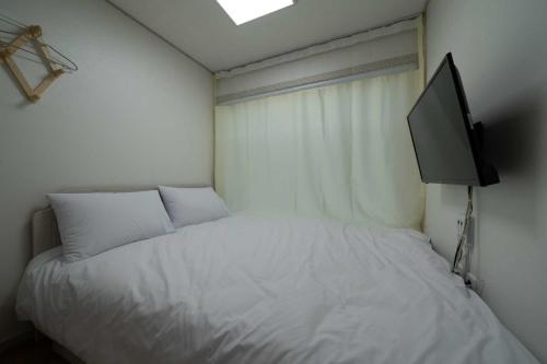 a bedroom with a white bed with a flat screen tv at Goseong Sustay Pension in Goseong