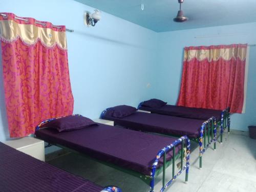 three beds in a room with red curtains at Square & Dormitory Stays in Tirunelveli