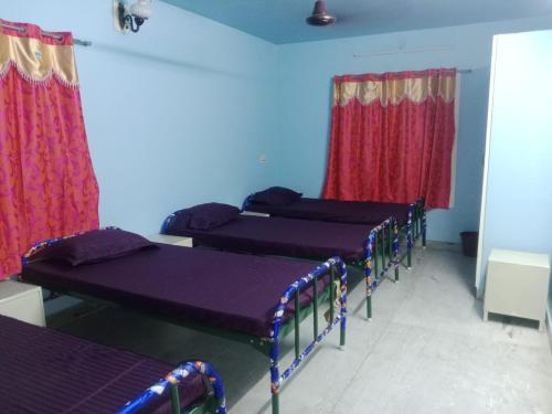 a row of beds in a room with red curtains at Square & Dormitory Stays in Tirunelveli