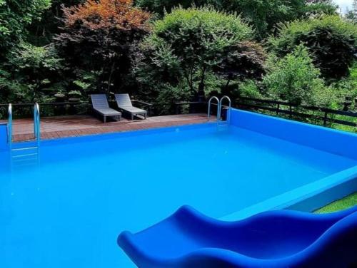 a blue pool with two chairs and trees at Hwacheon Myeongjiryeong Valley Pension in Hwacheon
