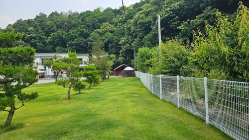a fence in a yard with trees and a house at Wonju Gwirae 630 Dog Pool Villa in Yongdang