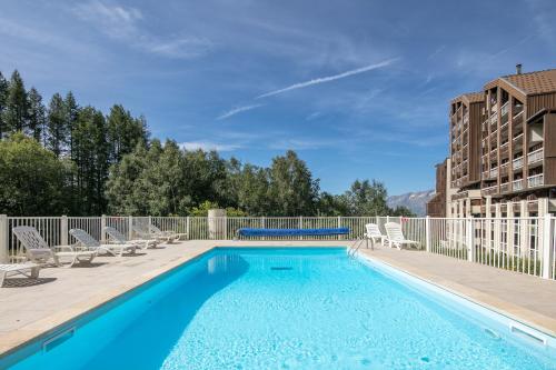 a swimming pool with chaise lounge chairs and a building at Résidence Pierre & Vacances Les Bergers in L'Alpe-d'Huez