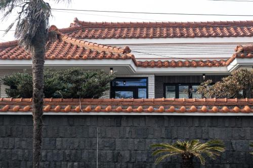 a house with a palm tree in front of a wall at Stay Hyeopjae Soop in Jeju