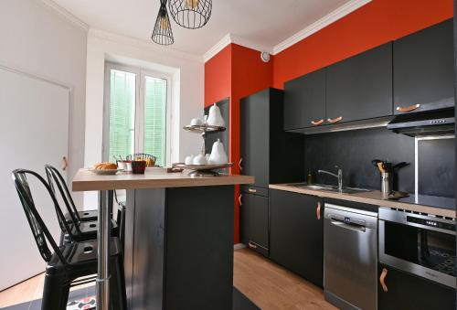 une cuisine avec des placards noirs et un mur aux accents orange dans l'établissement Maison climatisée Gare à 10 min, idéale familles MaisonCarréeConciergerie, à Nîmes