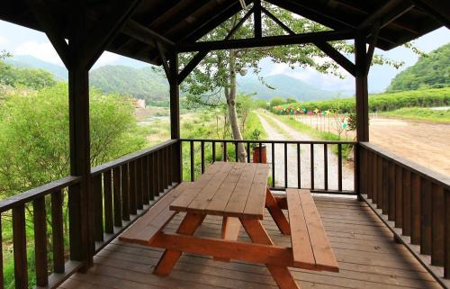 a wooden picnic table on a wooden deck with a view of a field at Cheongju Okhwadaestory Pension in Cheongju