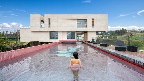 a woman standing in a swimming pool in front of a house at Jeju Mia Private Pool Villa large outdoor warm pool in Jeju