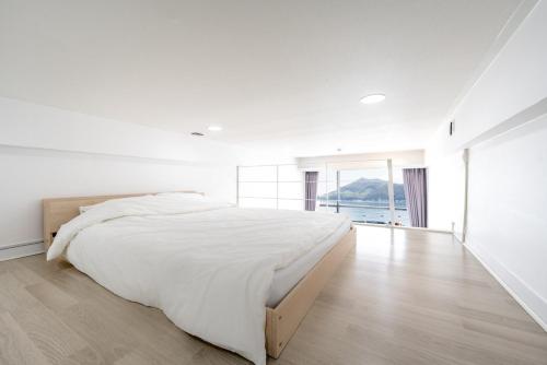 a white bedroom with a large bed and a large window at Namhae Red Wave Pension in Namhae