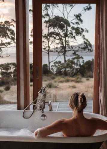 AlonnahにあるThe Hide private Waterfront on Beautiful Brunyの窓を見下ろす浴槽に横たわる女性