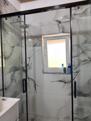 a bathroom with a glass shower with a window at Guest House Mali in Çorovodë