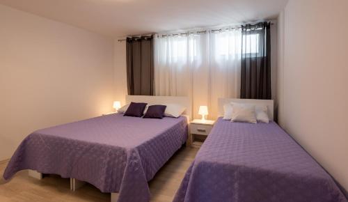two beds in a small room with purple sheets at Apartments Tanja & Josipa in Pag