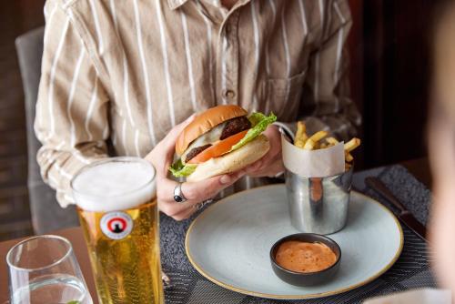 a person holding a sandwich and french fries and a beer at Thistle London Holborn in London