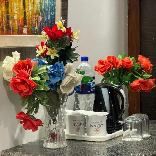 a vase of flowers on a counter with a bottle of water at Hotel Oban in Lahore