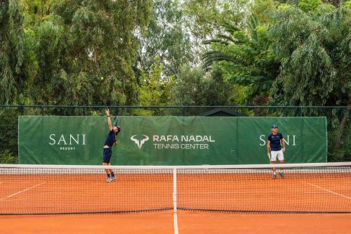 two people serving a tennis ball on a tennis court at Porto Sani in Sani Beach