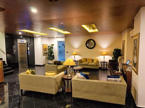 a lobby with couches and chairs and a clock at Hotel Oban in Lahore