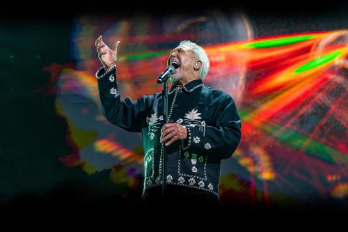 a man singing into a microphone on a stage at Porto Sani in Sani Beach