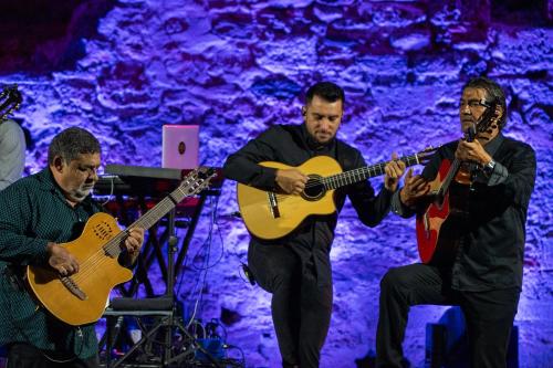 a group of three men playing guitars on a stage at Sani Club in Sani Beach