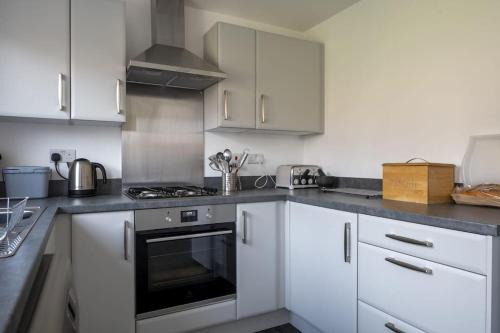 a kitchen with white cabinets and a stove top oven at Cosy 3 Bed Near Beaches, Cardiff & Brecon Beacons in Coity