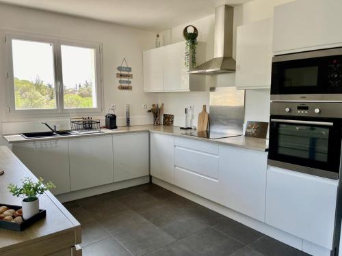 une cuisine blanche avec des armoires blanches et une fenêtre dans l'établissement Charmante maison vue garrigue avec piscine, à Lapalme