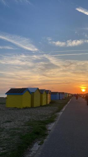 a row of beach huts with the sunset in the background at One-bedroom Apartment Sea Views in Rustington