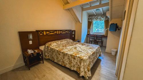 a bedroom with a bed and a table and a window at Hotel Pousada Ald' Mama in Gramado