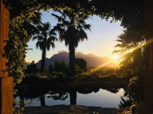 a sunset with palm trees and a body of water at Simunye Cottage in Simondium