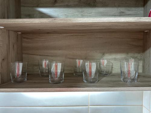 a row of glasses sitting on a wooden shelf at MM Apartman in Stara Pazova